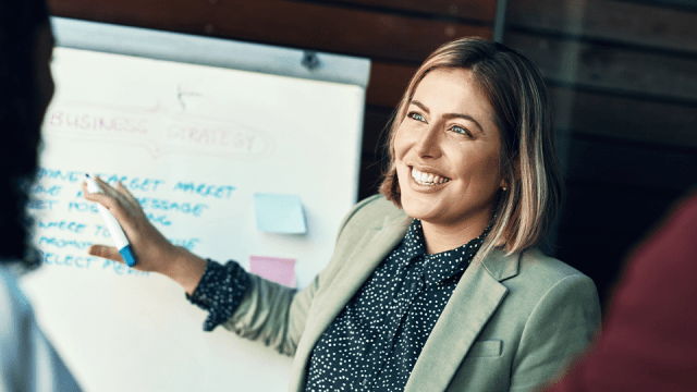 A smiling woman stands in front of a whiteboard as she goes over learning opportunities within her accounting firm.