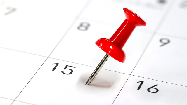 A red thumbtack pierces a calendar on the 15th of the month to indicate a deadline.