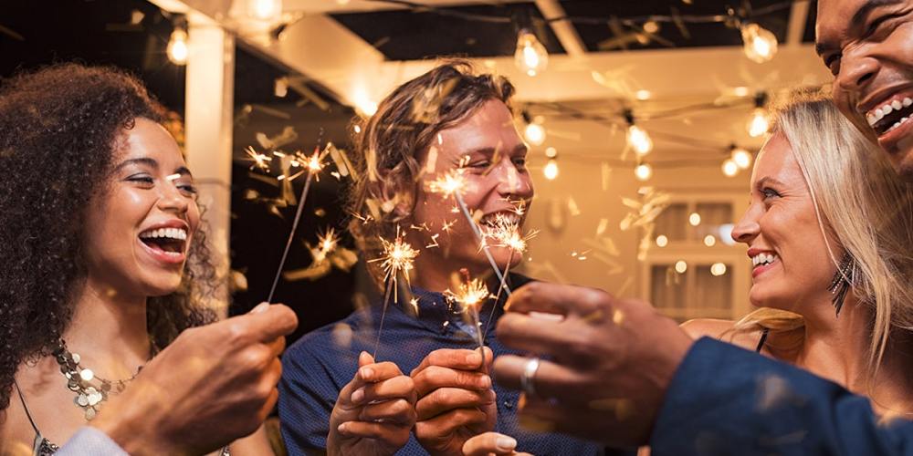 A group of smiling accounting firm staff hold sparklers while celebrating the new year, knowing their accounting firm's New Year's resolutions are setting them up for success.