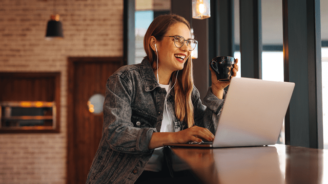 A woman sits at a coffee shop with her laptop, sipping on a cup of coffee.