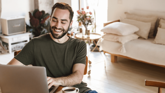 A smiling man is happy as he works on his laptop from home.