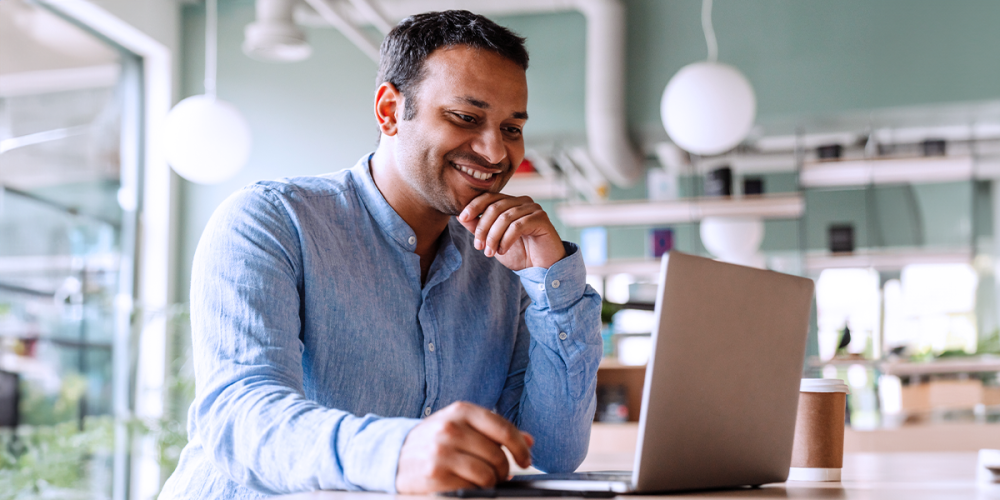 A man sits in front of his laptop smiling as he easily reviews emails he sent from QuickBooks