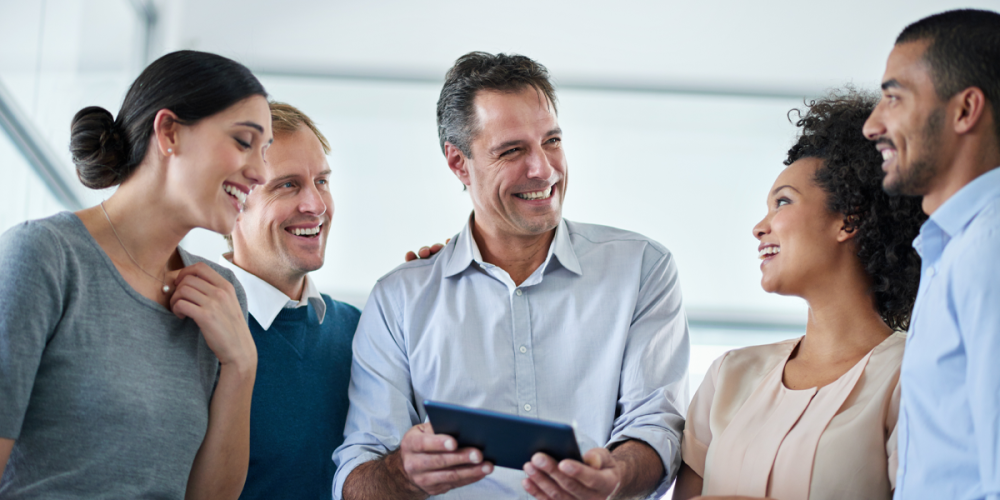 A group of employees stand smiling at each other. One in the middle holds a tablet to show what he learned about security for accounting firms.