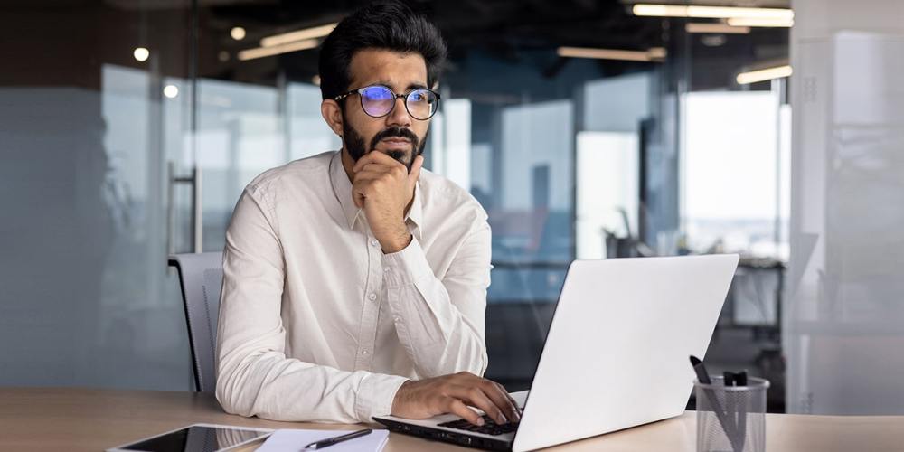 A man sits in front of a laptop as he ponders ways to find new employees.