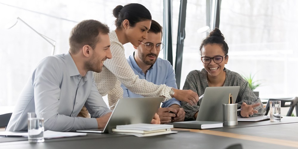 A small group of people sit at a table with two laptops open in front of them as they look at those, one pointing at a screen, considering their next step as a result of the QuickBooks Desktop 2024 pricing increases