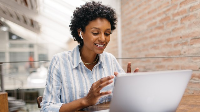 An image with a woman working at her laptop with an AirPod in her ear, smiling as she talks to someone at Rightworks to get help in her decision of what to do with the QuickBooks changes.