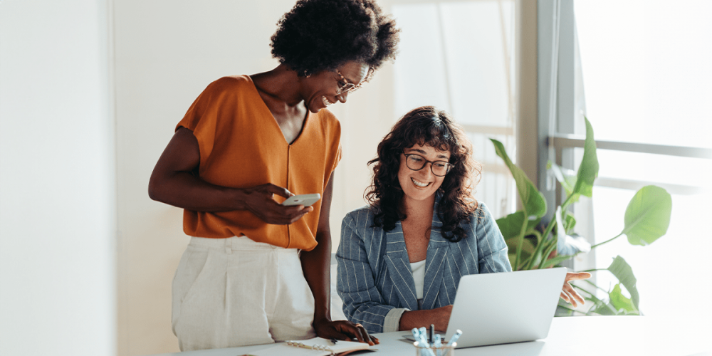 Two coworkers chat in front of a laptop as they discuss their companies positive culture.