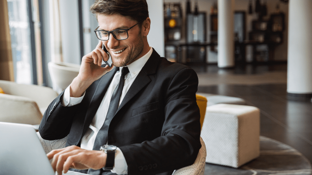 A smiling employee sits in front of a laptop speaking on the phone.