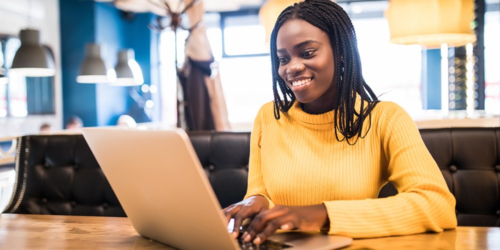 A smiling woman sits in front of a laptop typing as she accesses her client management apps in OneSpace.