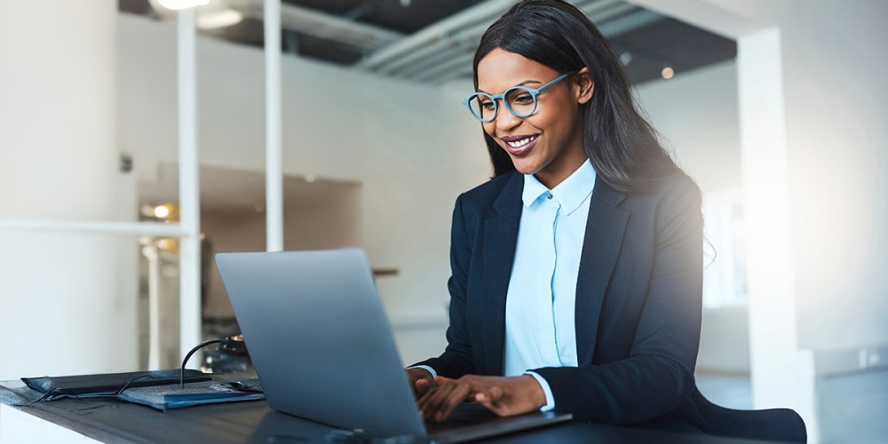 A smiling woman sits at a desk, researching RAM minimum requirements.