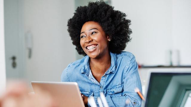 A woman sits in front of a laptop looking content because she knows her employer prioritizes cybersecurity.