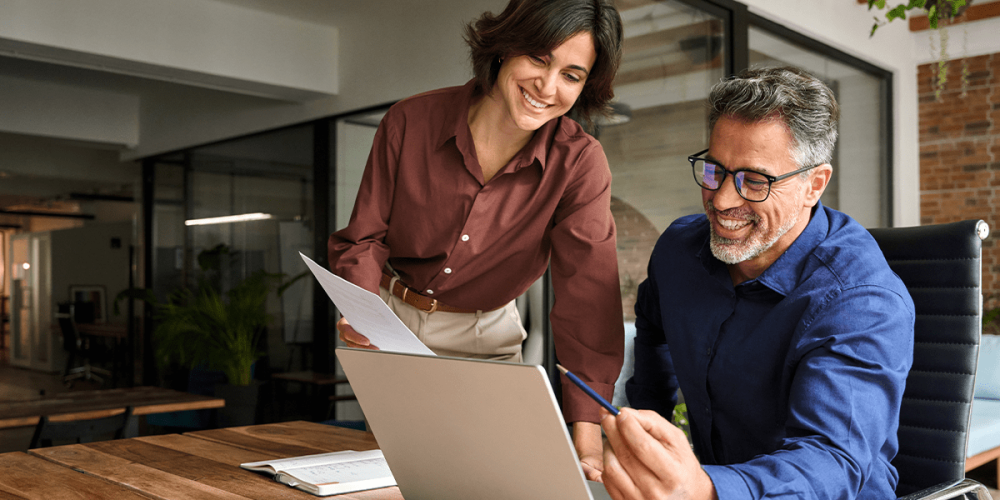 A man and woman work together in an office, going over the process they have in place for software patch management.