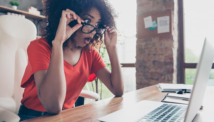 A woman looks at her laptop in shock.