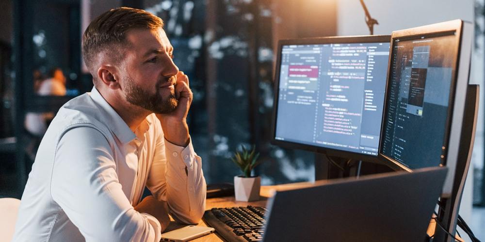 A man sits looking at multiple display monitors, confident that he has the tax season technology tools that he needs.